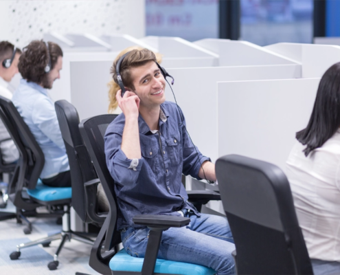 A young person smiling while on the phone at a help desk job.