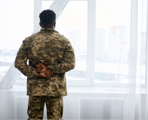 A veteran man in an army uniform looking out a window.