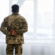 A veteran man in an army uniform looking out a window.
