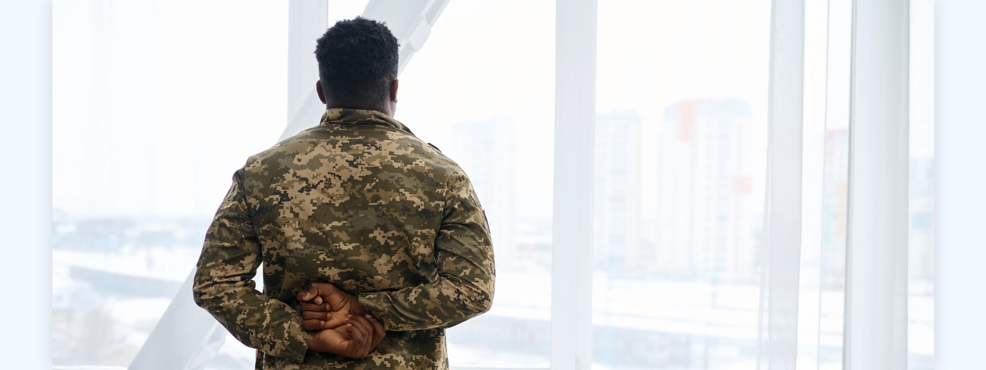 A veteran man in an army uniform looking out a window.