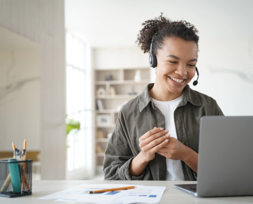 An office worker wearing a headset smiles while sitting at her computer.