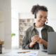 An office worker wearing a headset smiles while sitting at her computer.