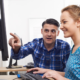A man gives a female employee IT training at a computer.